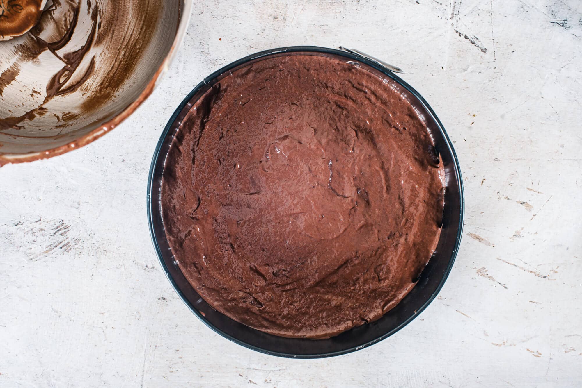 chocolate-cake-batter-in-a-springform-pan-with-an-empty-silver-bowl-on-the-side