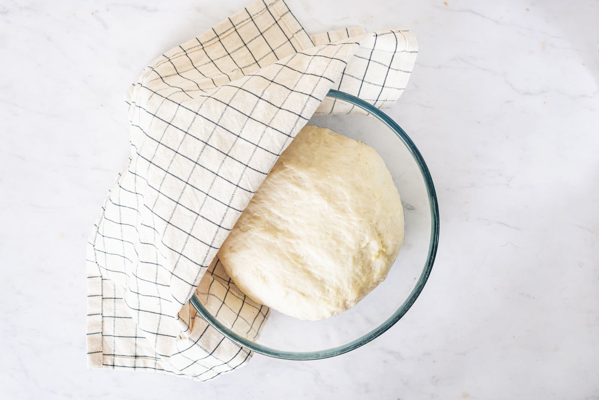 dough-in-a-glass-bowl-half-covered-by-a-white-towel