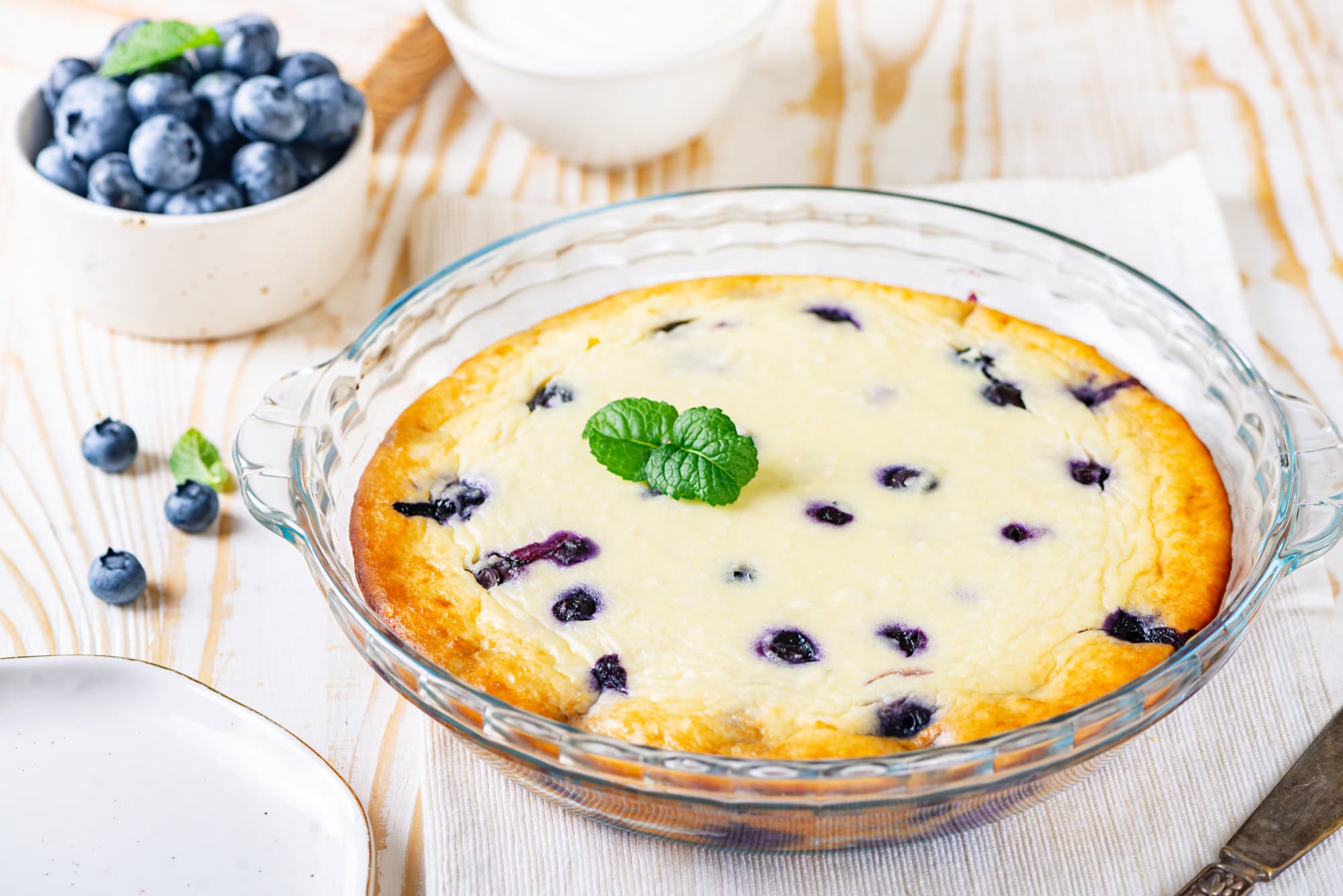 blueberry-cake-in-a-glass-dish-on-a-white-towel-with-a-bowl-of-blueberries-on-the-side