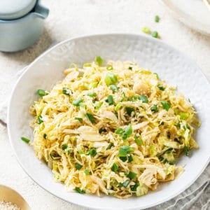 cabbage-salad-in-a-white-bowl-with-a-bowl-of-sesame-seeds-on-the-side-and-green-onion-in-the-background