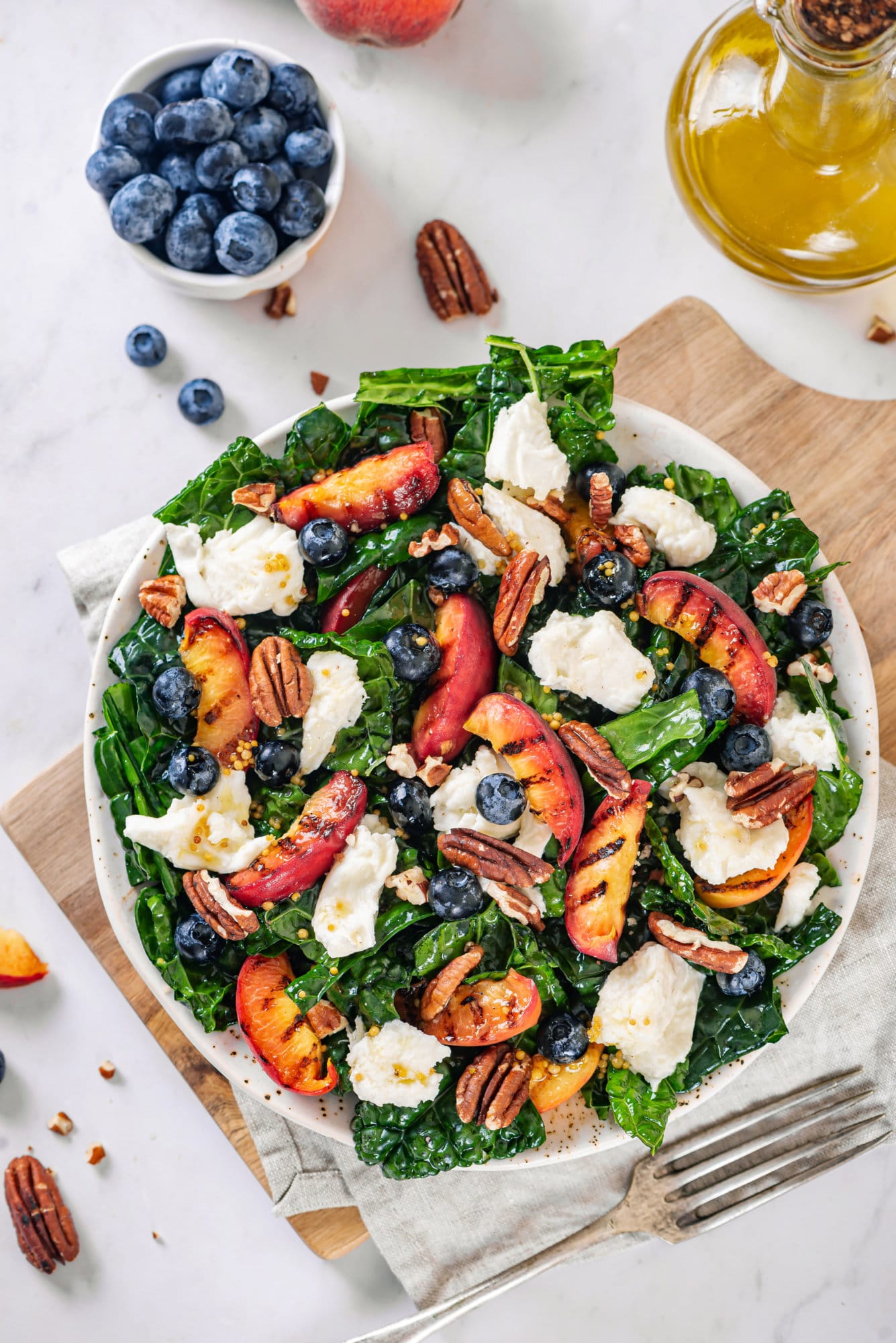 Grilled peaches and kale salad with blueberries and walnuts all mixed together in a bowl.