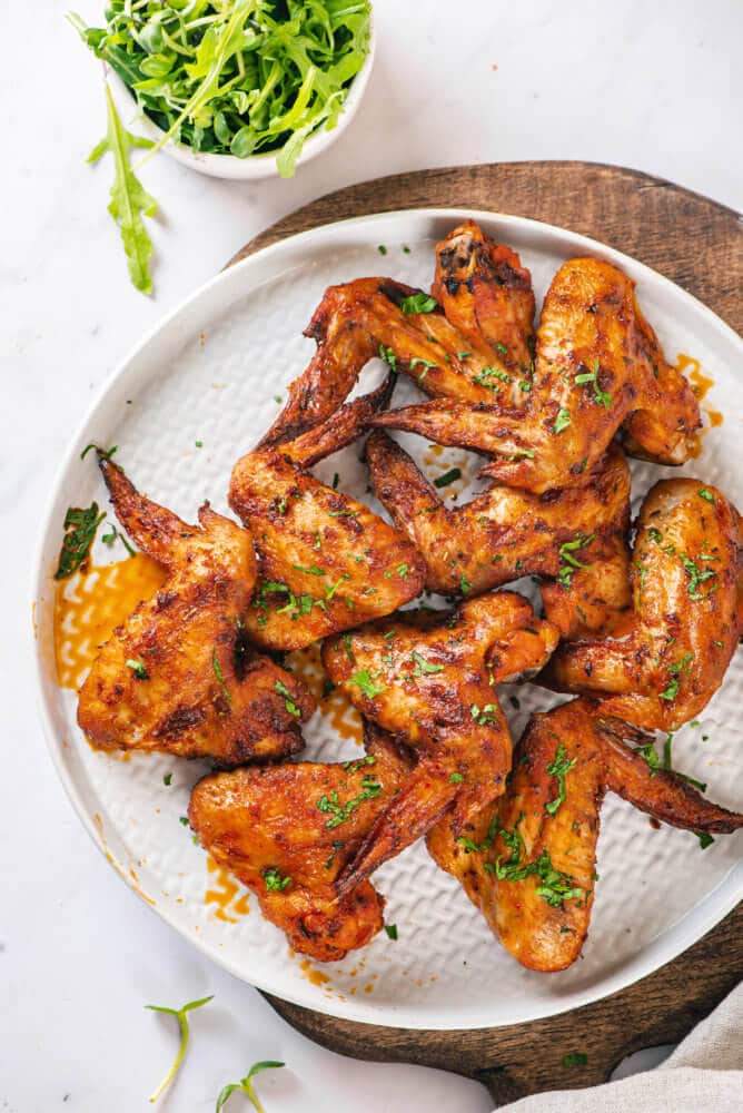 chicken-wings-on-a-white-plate-on-a-wooden-board-with-arugula-on-the-side