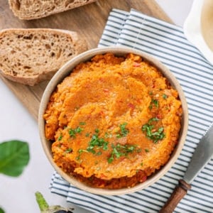 spread-in-a-brown-bowl-on-a-blue-towel-with-a-wooden-board-with-bread-slices-on-the-side-and-an-eggplant-and-a-spreading-knife-on-the-side