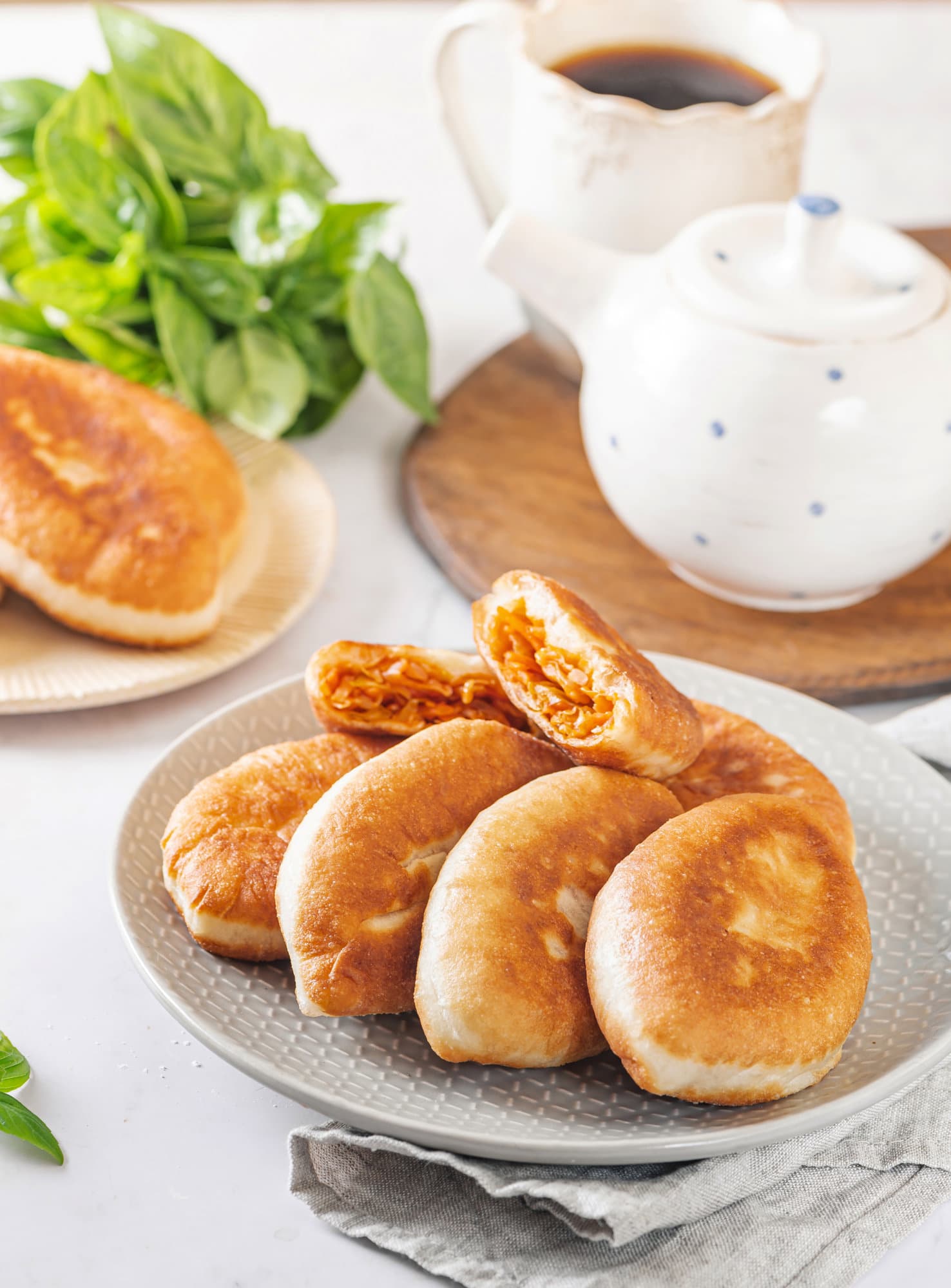 piroshki-with-cabbage-on-a-white-speckled-plate-with-a-teapot-and-a-mug-of-tea-in-the-background-on-a-wooden-board