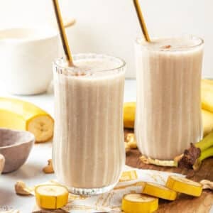 Banana bread smoothie atop a wooden board with cashews and bananas on the side.