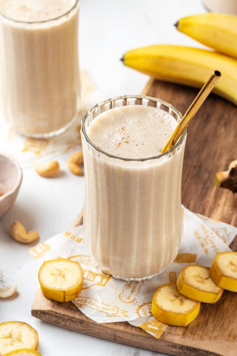 Banana protein smoothie with a gold straw, and bananas on the side.