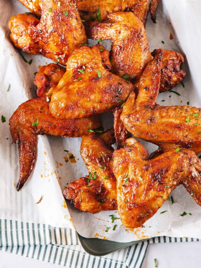 chicken wings on parchment paper tray on a striped towel with arugula on the side.