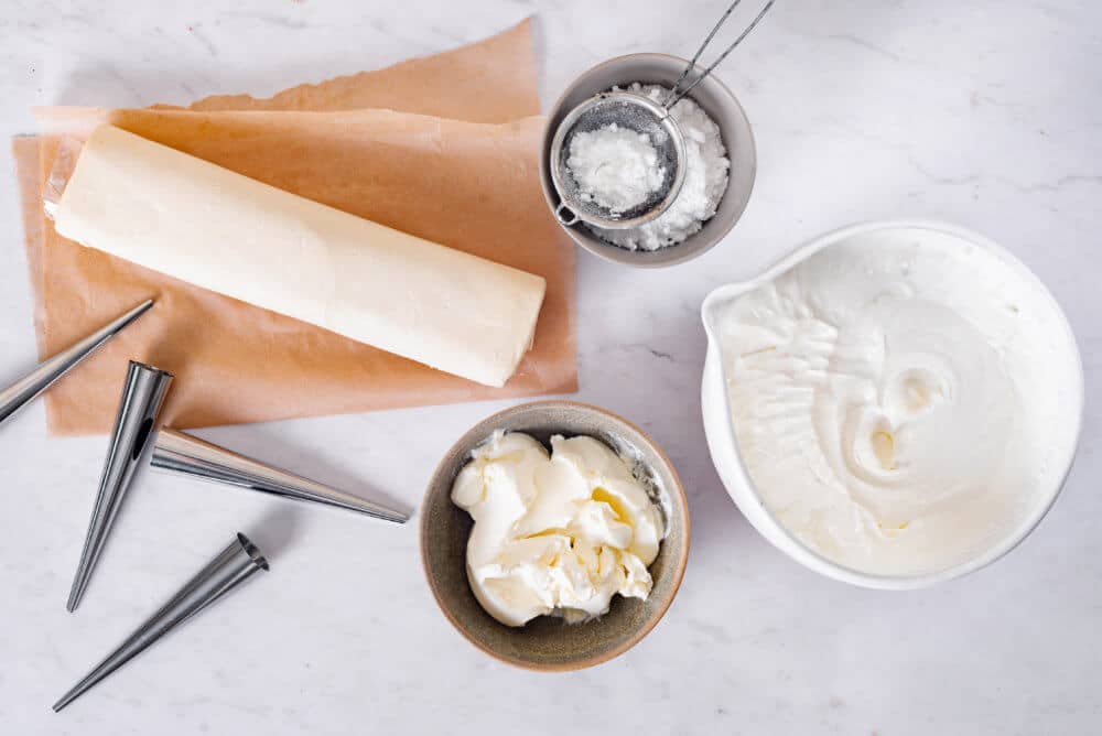 puff-pastry-cream-horns-ingredients-and-equipment-cream-cheese-cool-whip-puff-pastry-dough-powdered-sugar-a-sifter-cream-horn-molds-and-parchment-paper
