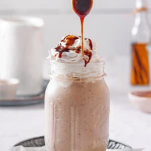 caramel-smoothie-in-a-mason-jar-with-a-striped-straw-on-a-black-plate-with-a-spoon