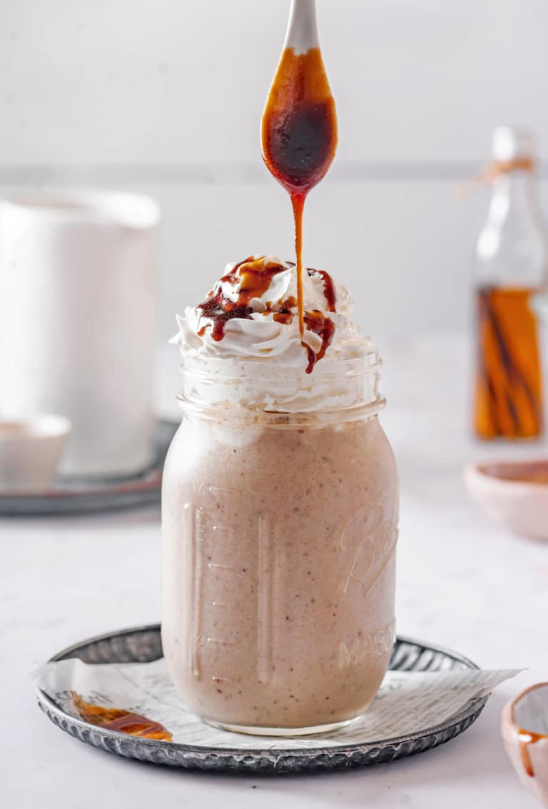 caramel-smoothie-in-a-mason-jar-with-a-striped-straw-on-a-black-plate-with-a-spoon