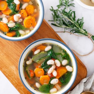 tuscan-soup-in-a-bowl-on-a-wooden-board-with-a-spoon-and-rosemary