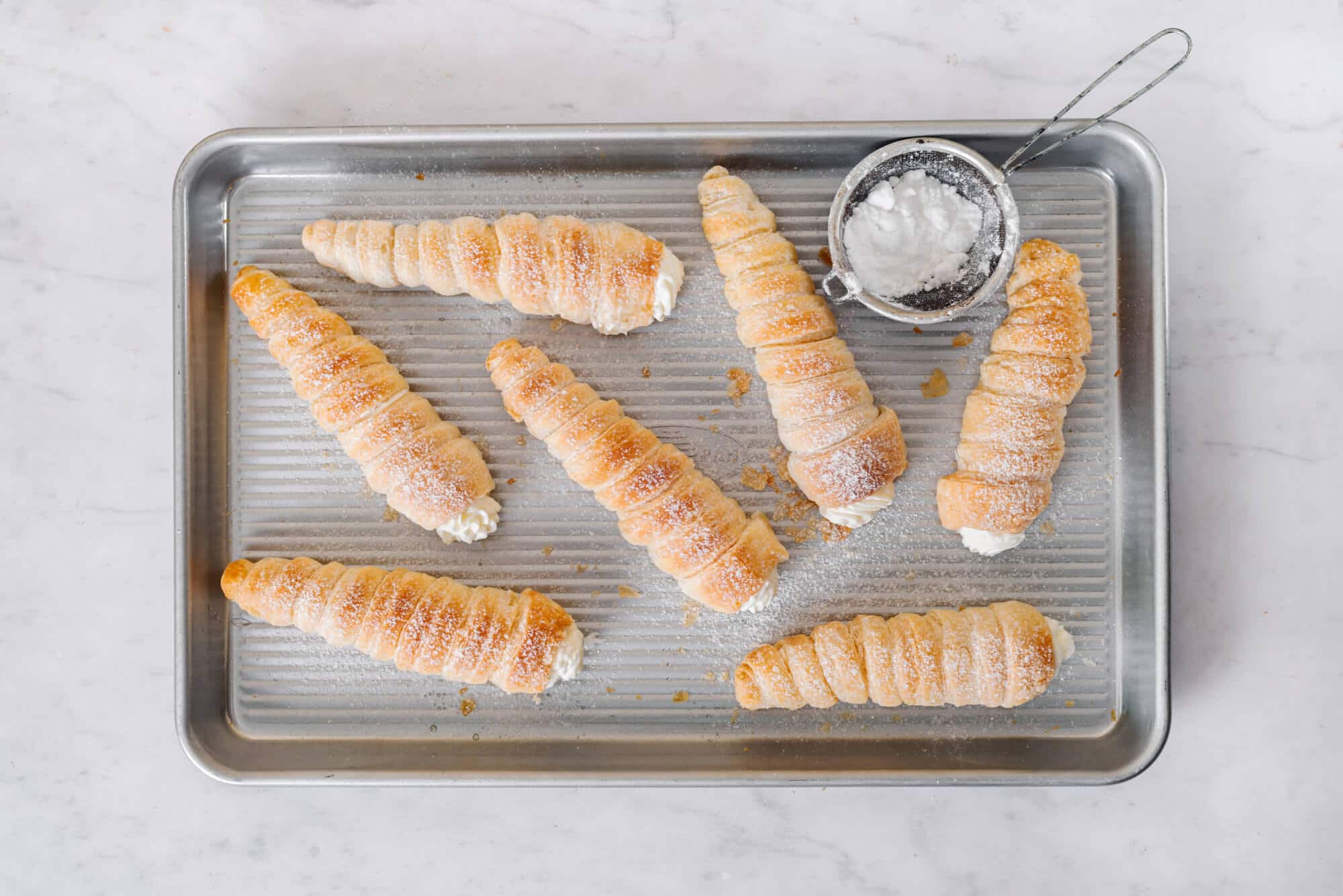 A baking tray with cream horns dusted with powdered sugar.