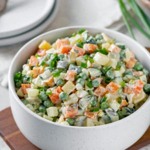 Olivier salad in a white bowl on a wooden board.