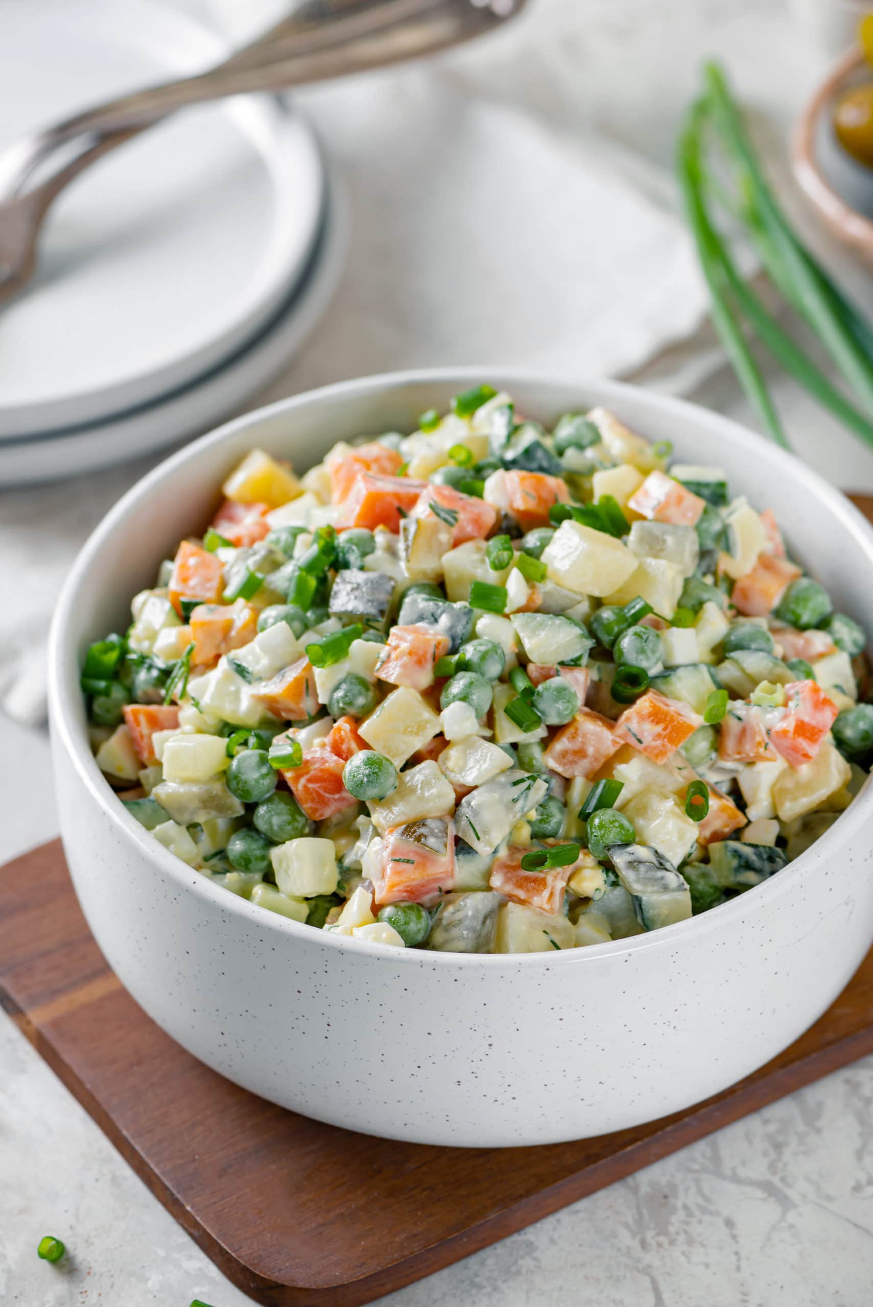 Olivier salad in a white bowl on a wooden board.