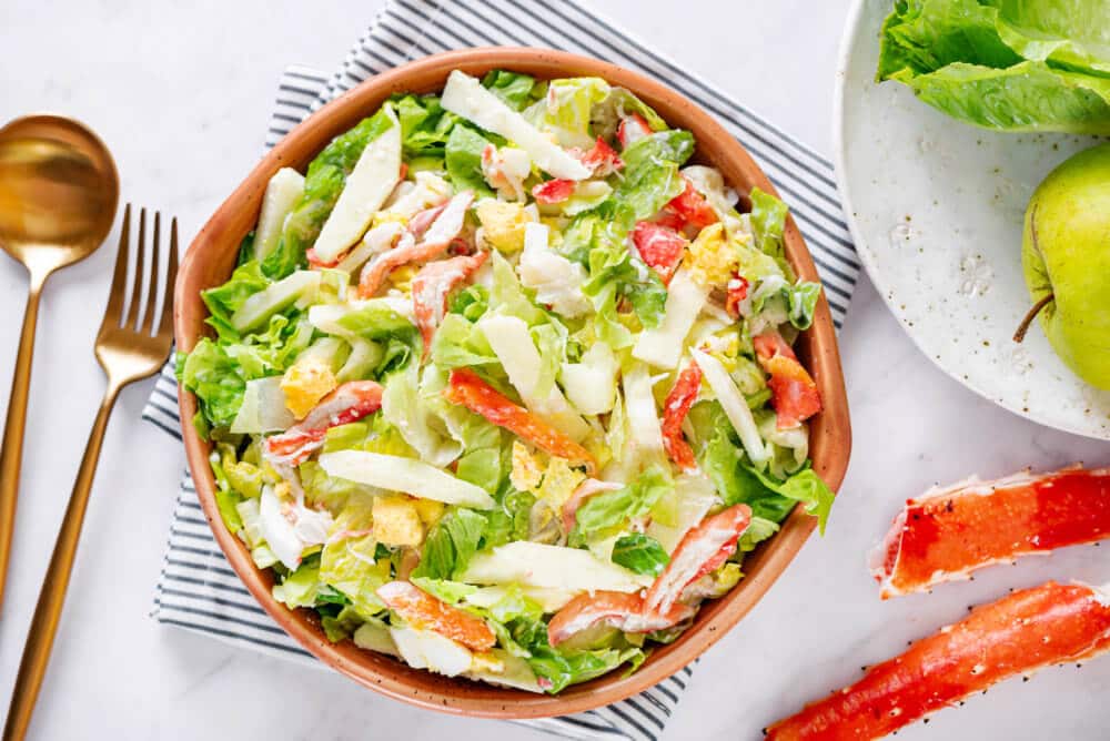 crab and apple salad in a brown bowl atop a striped dark blue towel.