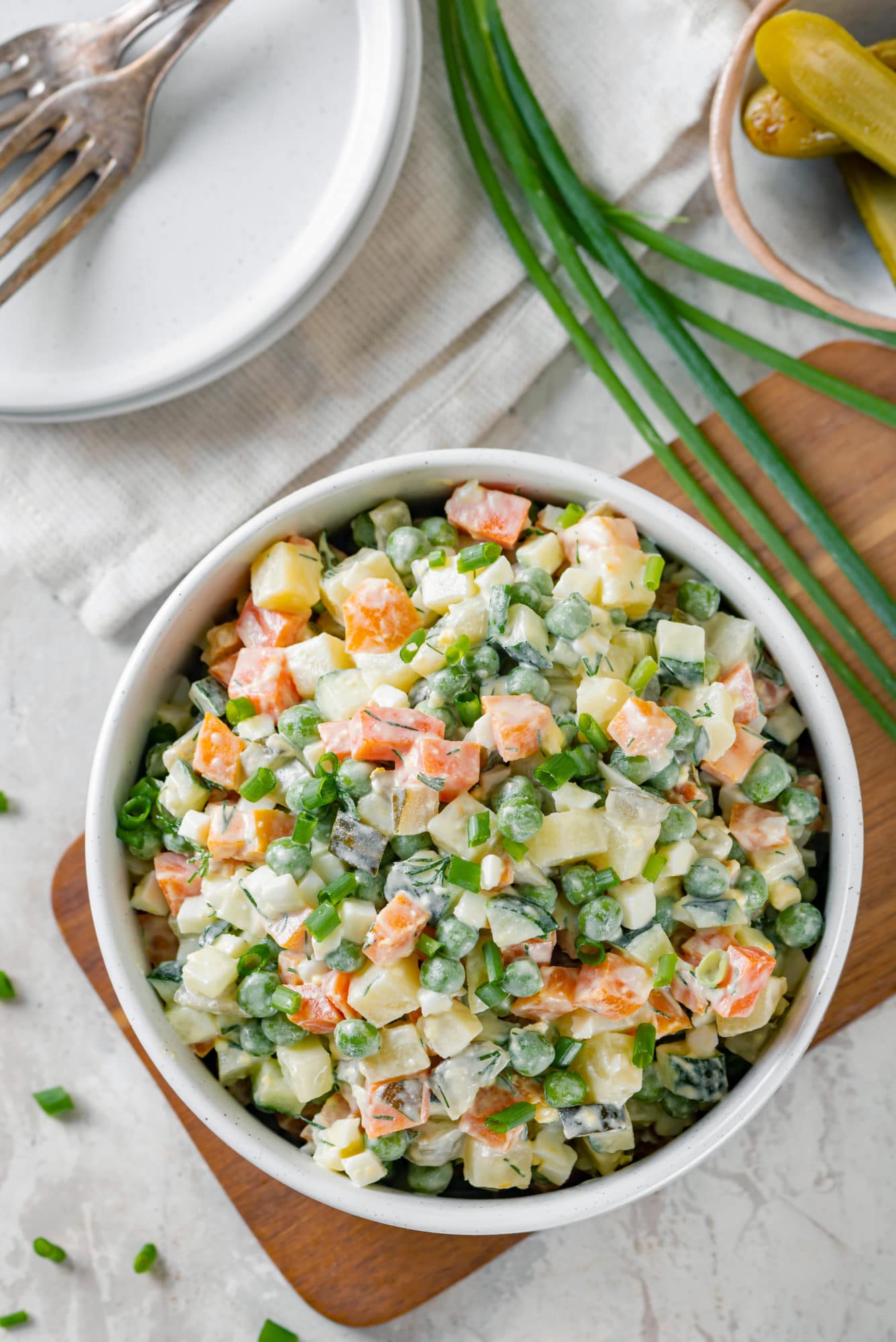 olivier-salad-in-a-white-bowl-on-a-wooden-board-with-green-onion