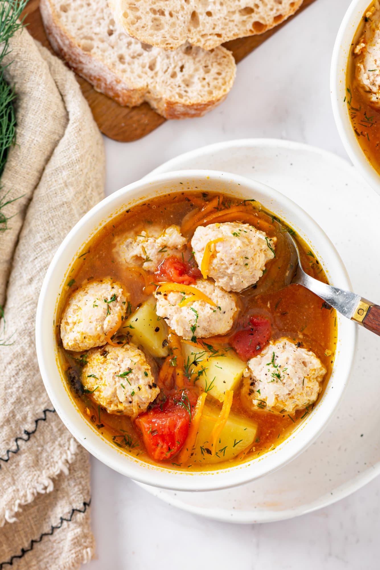 tomato-chicken-soup-in-a-white-bowl-on-a-white-plate-with-a-spoon