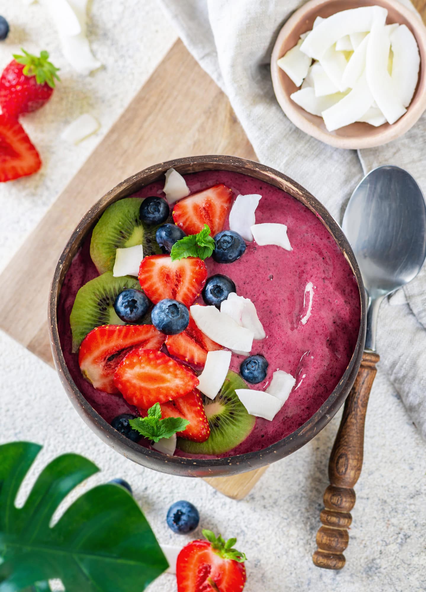 Acai smoothie in a brown bowl with toppings and a spoon on the side. 