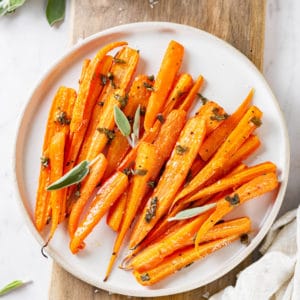 roasted-carrots-on-a-white-plate-on-a-wooden-board-with-sage