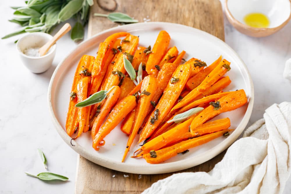 roasted-carrots-on-a-white-plate-on-a-wooden-board-with-sage