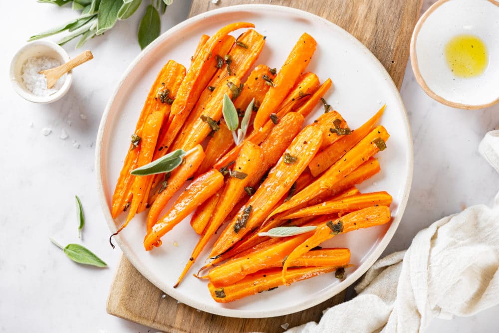 roasted carrots with sage on a white plate.