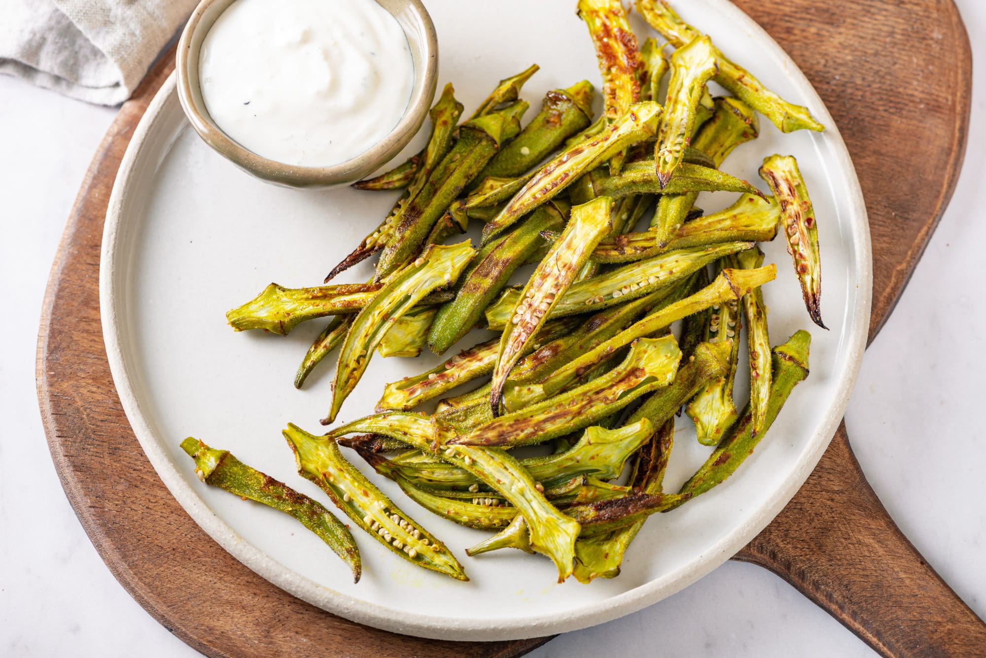 roasted-okra-on-a-white-plate-and-a-wooden-board-with-a-bowl-of-dip-on-the-side