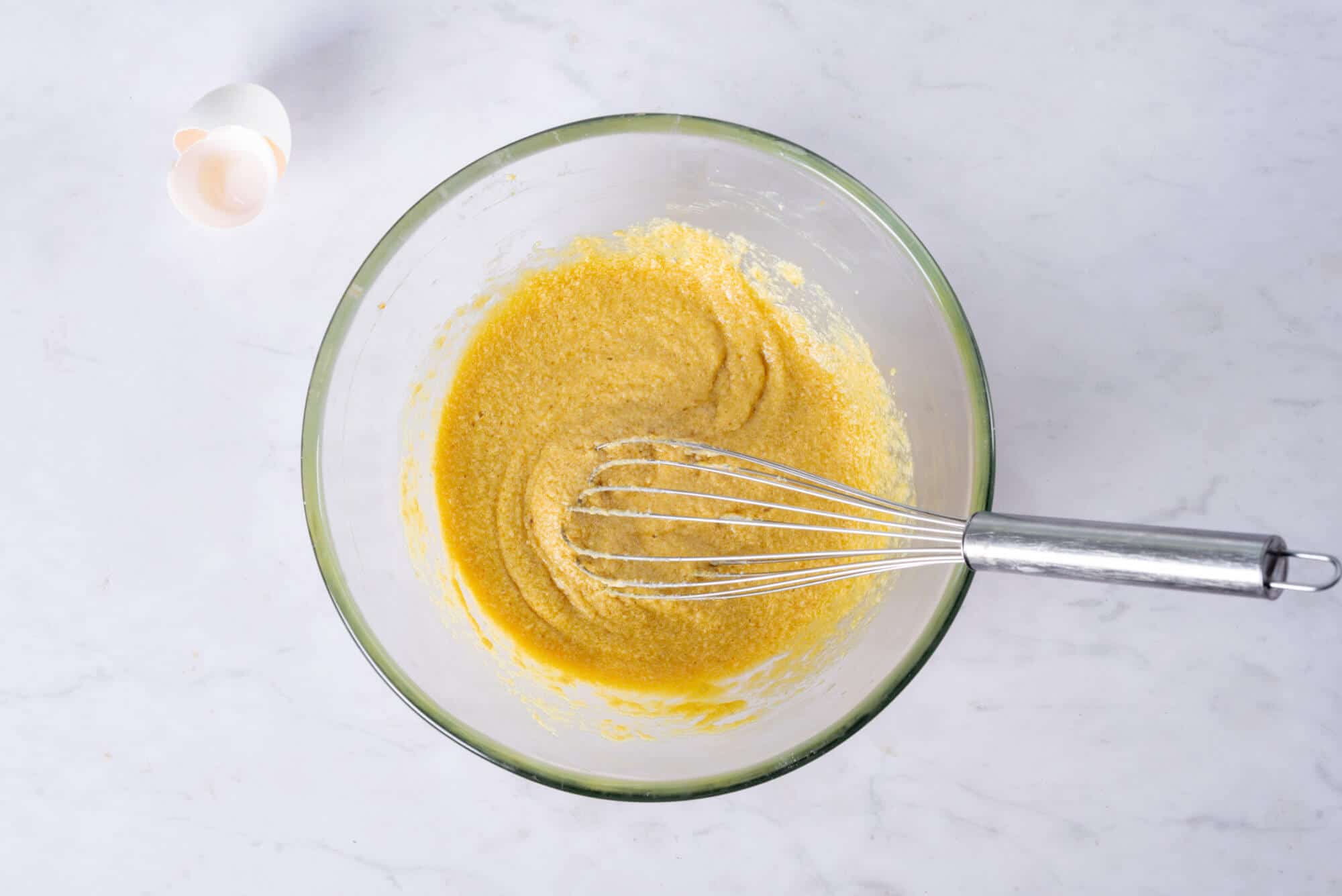 plum-cake-batter-in-a-clear-bowl-with-a-whisk-and-eggshells-on-the-side