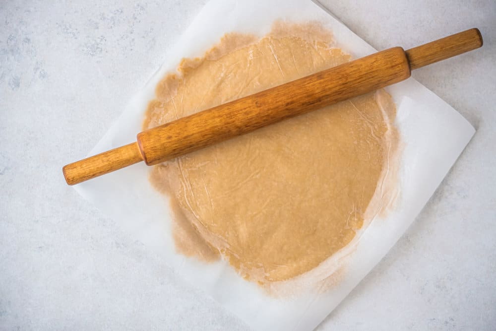 dough-for-apple-tart-under-parchment-paper-and-a-rolling-pin