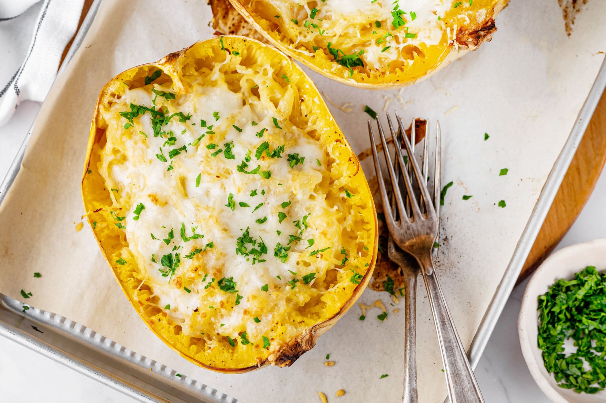 Spaghetti squash on a baking tray with creamy sauce with forks ready to serve.