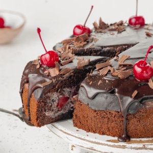 cherry-chocolate-cake-on-a-white-cake-stand-with-a-slice-of-cake-on-a-spatula