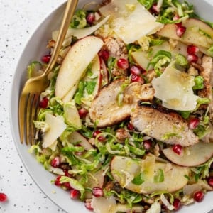 Brussels sprouts salad in a white bowl with a gold fork on the side.