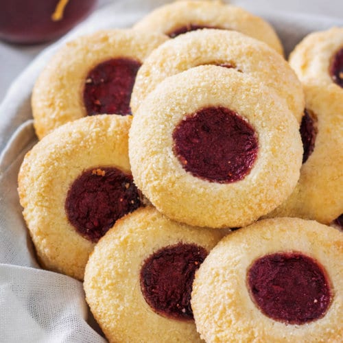 A selection of thumbprint cookies in a bowl with a towel.
