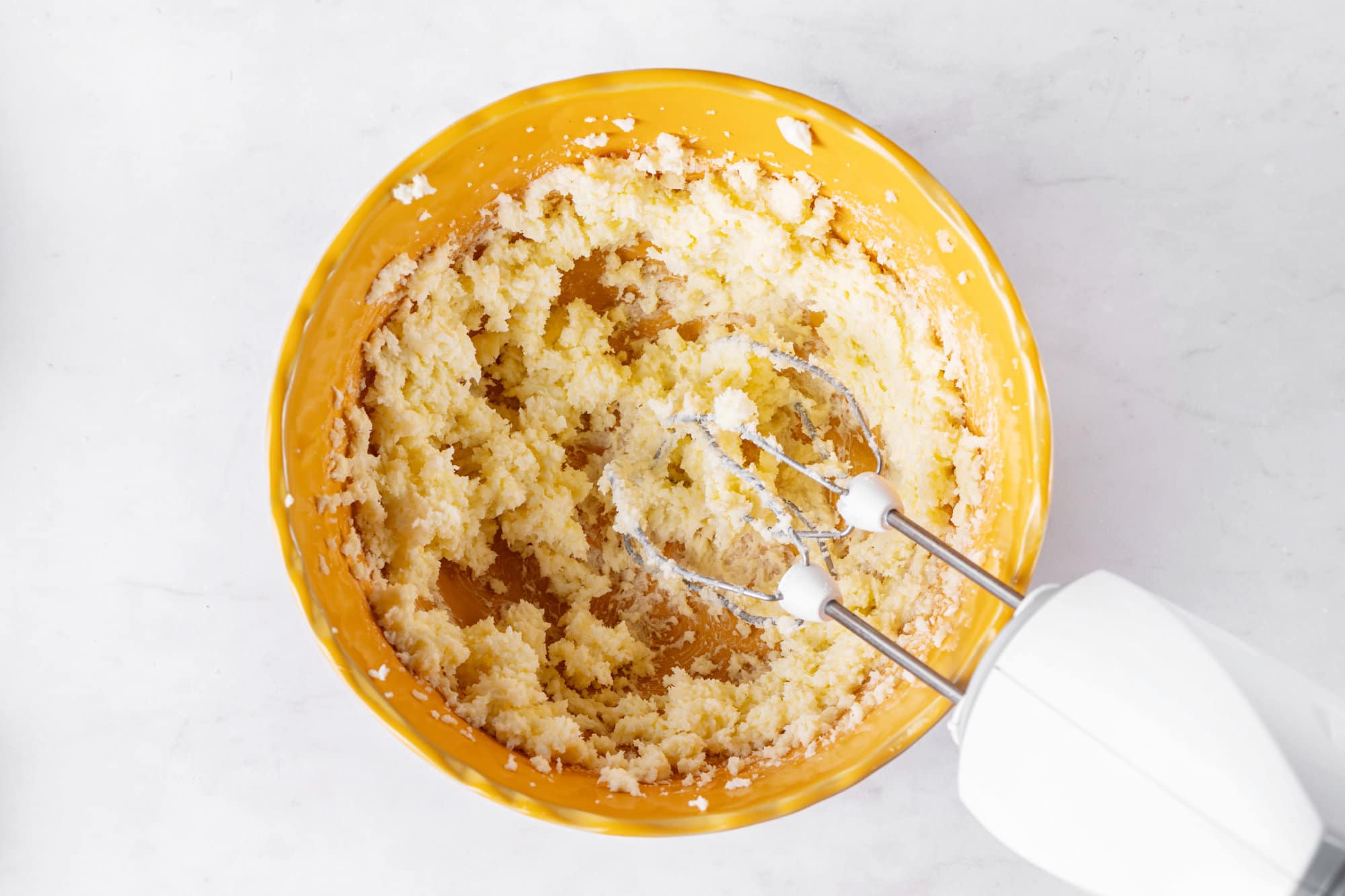 Creaming butter and sugar in a yellow bowl with hand mixers.