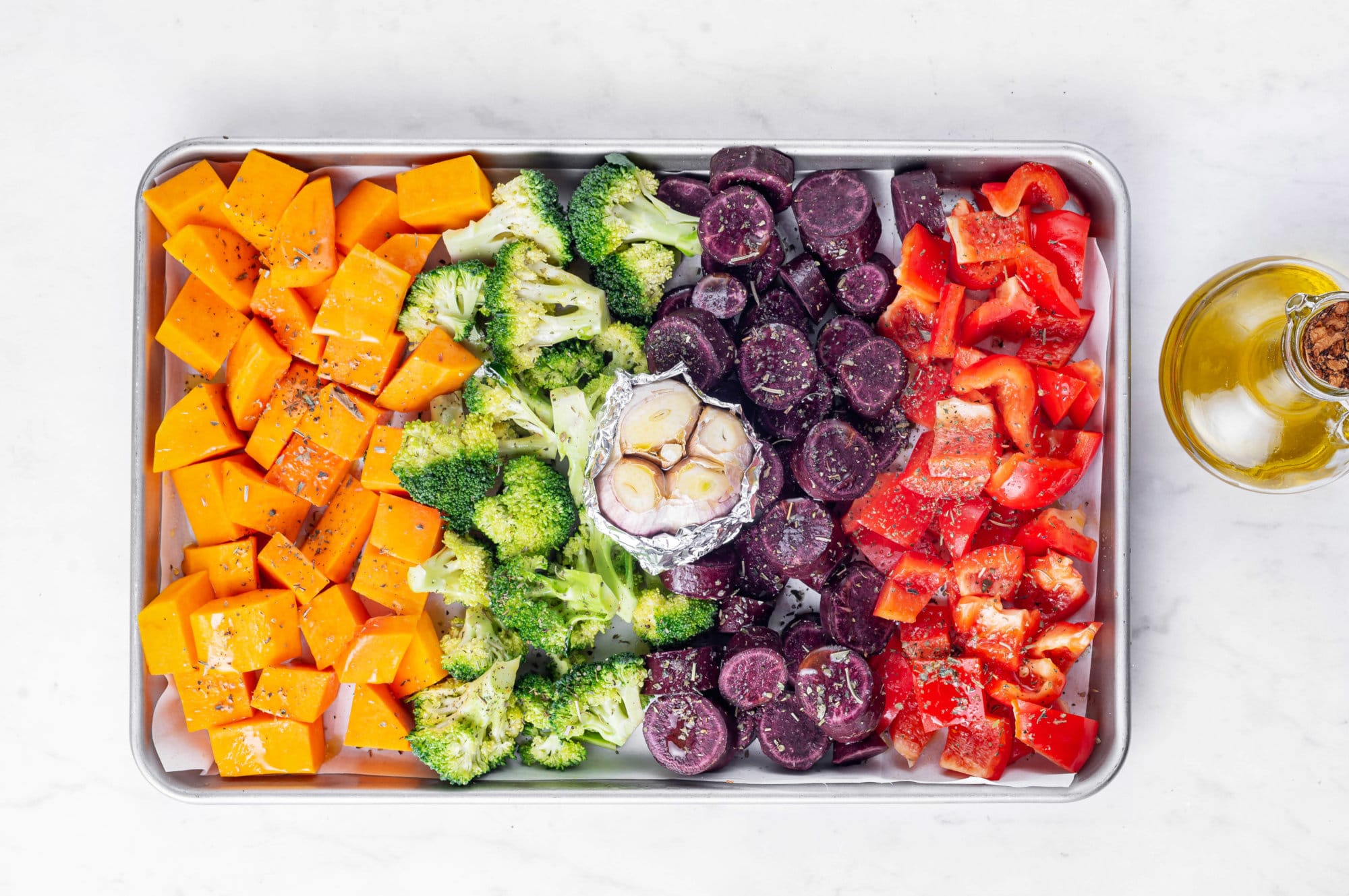Roasted Vegetables in the Oven with Easy Roasted Garlic Lemon Dressing roasted veggies on a baking tray with roasted garlic wrapped in foil in the center.