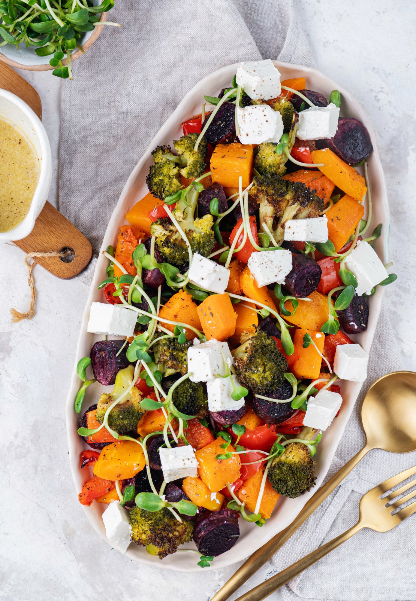 Roasted Vegetables in the Oven with Easy Roasted Garlic Lemon Dressing roasted vegetables in a large dish with dressing in a bowl on the side.