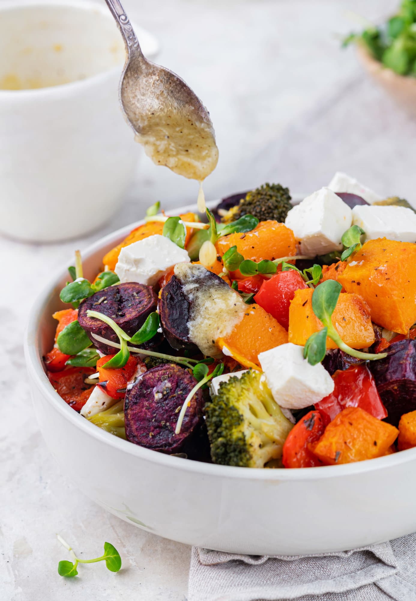 Roasted Vegetables in the Oven with Easy Roasted Garlic Lemon Dressing a spoon drizzling dressing atop roasted veggies with fresh microgreens on top.