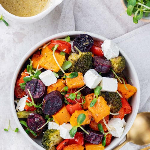 roasted-vegetables-in-white-bowl-with-gold-fork-and-spoon-and-bowl-of-dressing-on-the-side