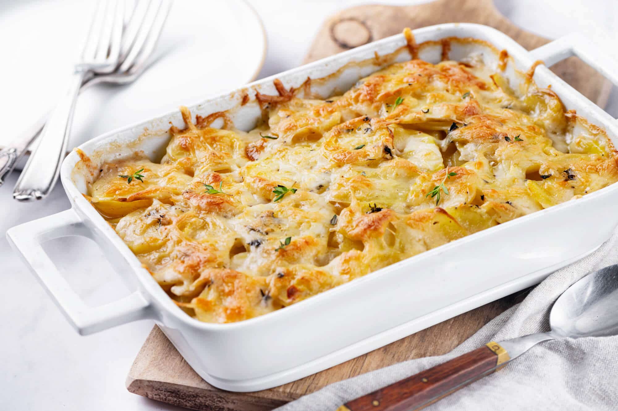 a white baking dish filled with baked scalloped potatoes with melted cheese on top.