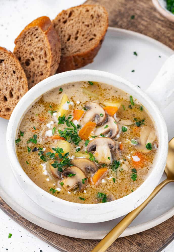 a white bowl of mushroom soup with slices of bread and a spoon on the side.