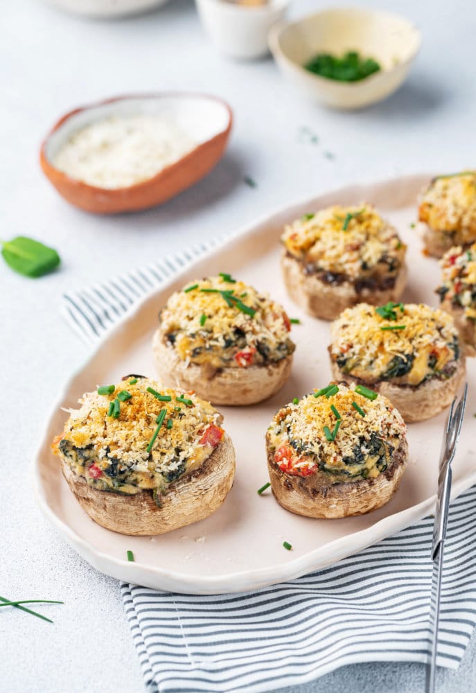 stuffed-mushroom-bites-on-beige-plate-with-striped-towel-and-tongs