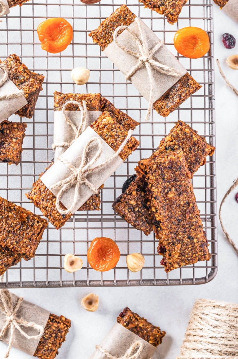 Stacks of fruit and nut bars on a wire rack with more dried fruit and nuts on the side.