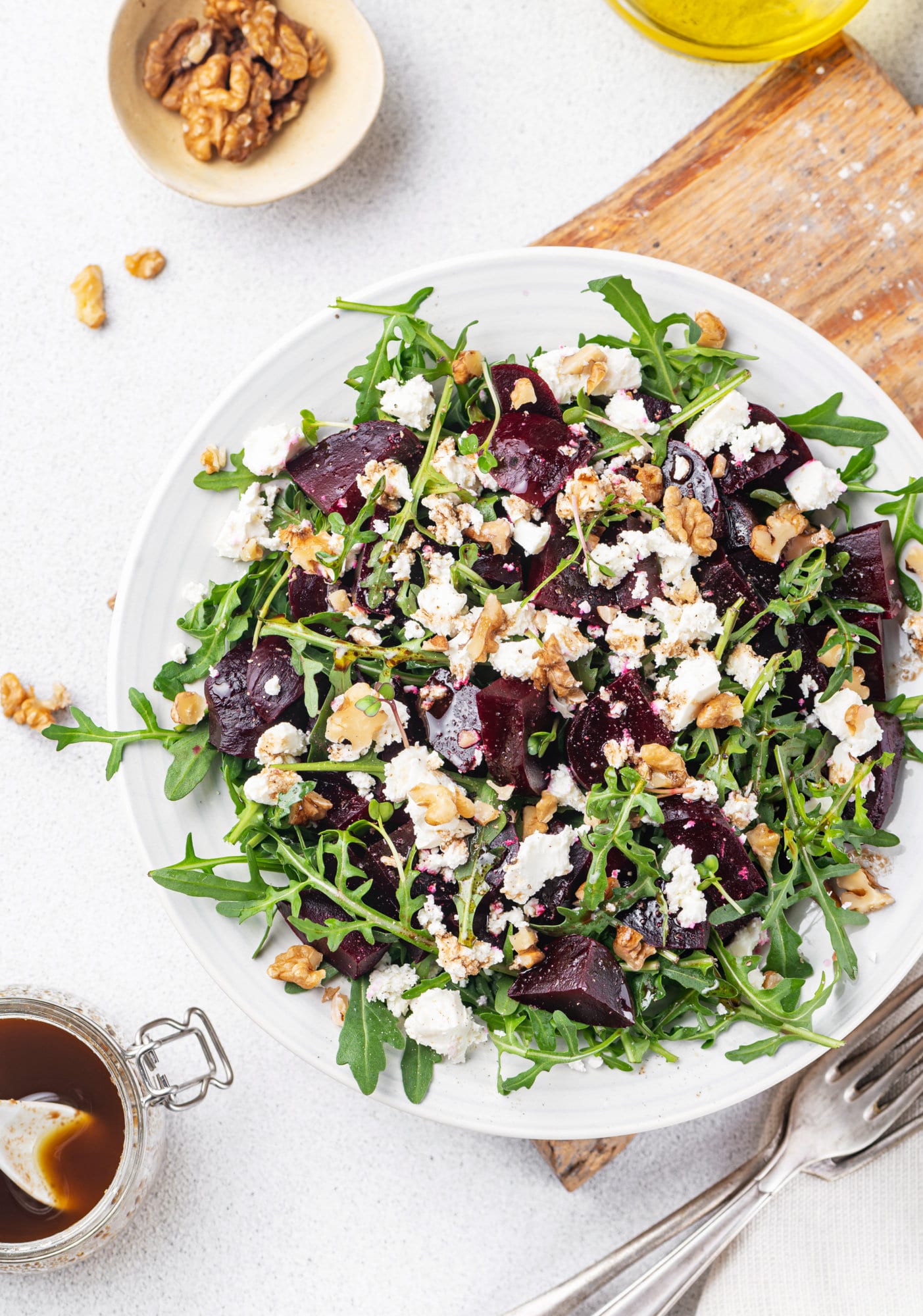 beet-salad-on-a-white-plate-and-wooden-board-with-cheese-and-arugula-with-forks-and-walnuts