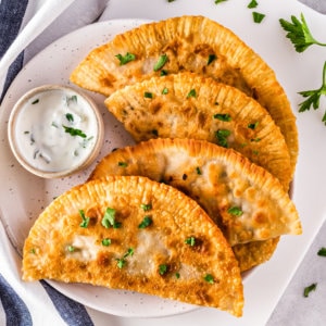 Chebureki with cilantro on a white plate with a dip on the side.