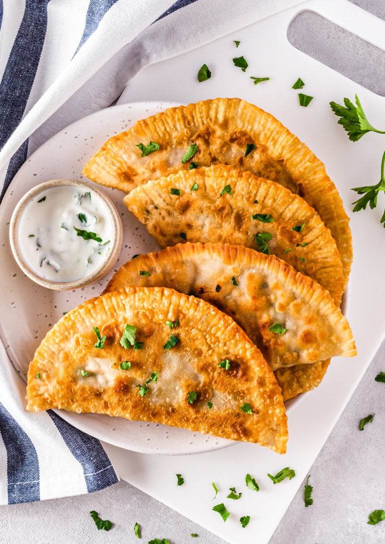 Chebureki with cilantro on a white plate with a dip on the side.