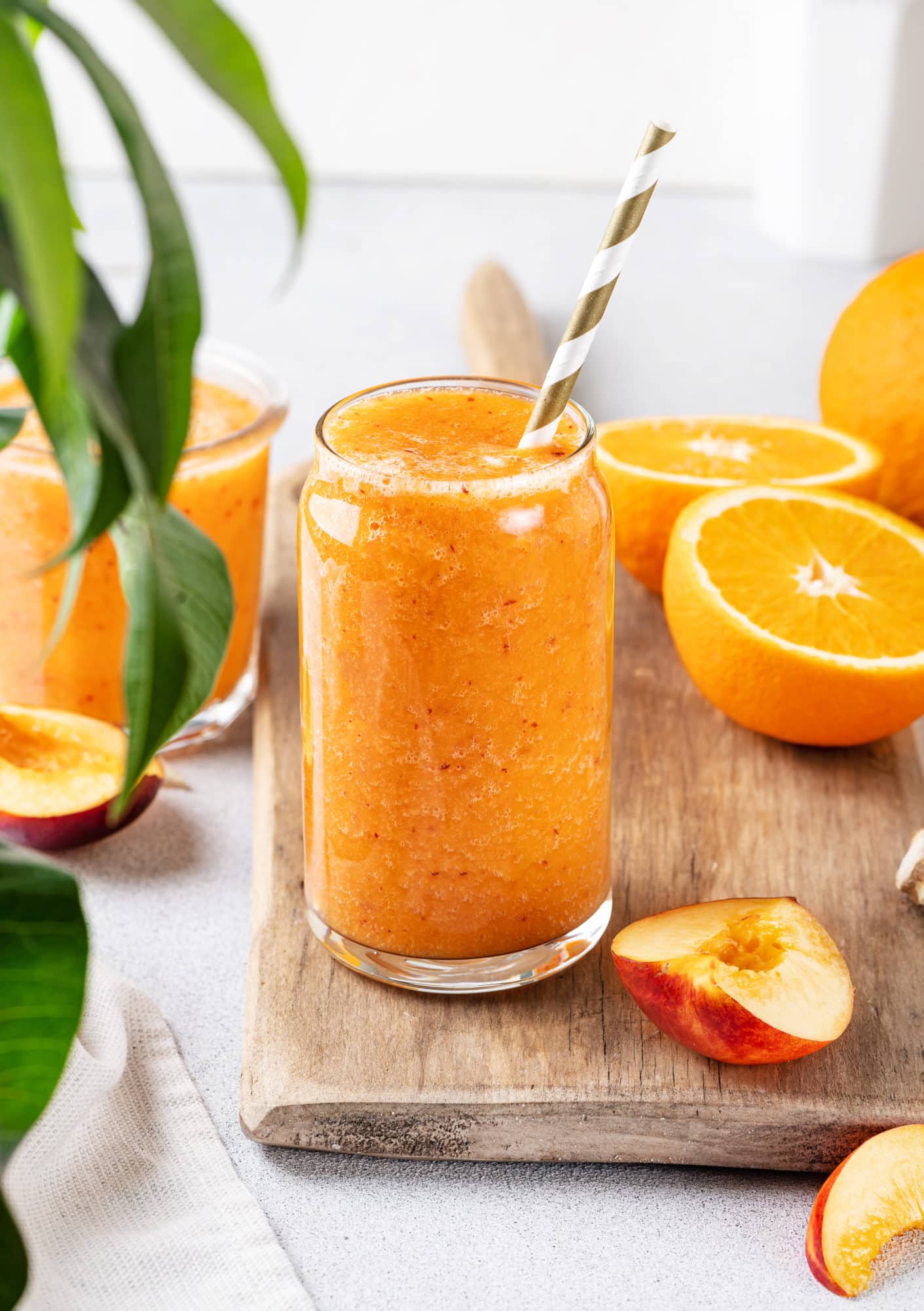 apricot-smoothie-carrot-juice-in-clear-glass-on-wooden-board-sliced-orange-brown-white-straw-green-leaves