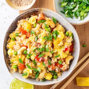 pineapple fried rice in a grey bowl with scallions on top and chopsticks on the side.