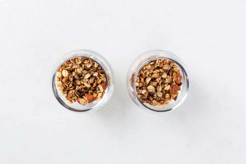 Two glass parfait glass with granola on top.