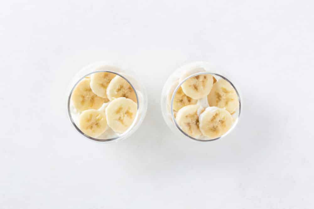 Two glass parfait cups with sliced bananas.
