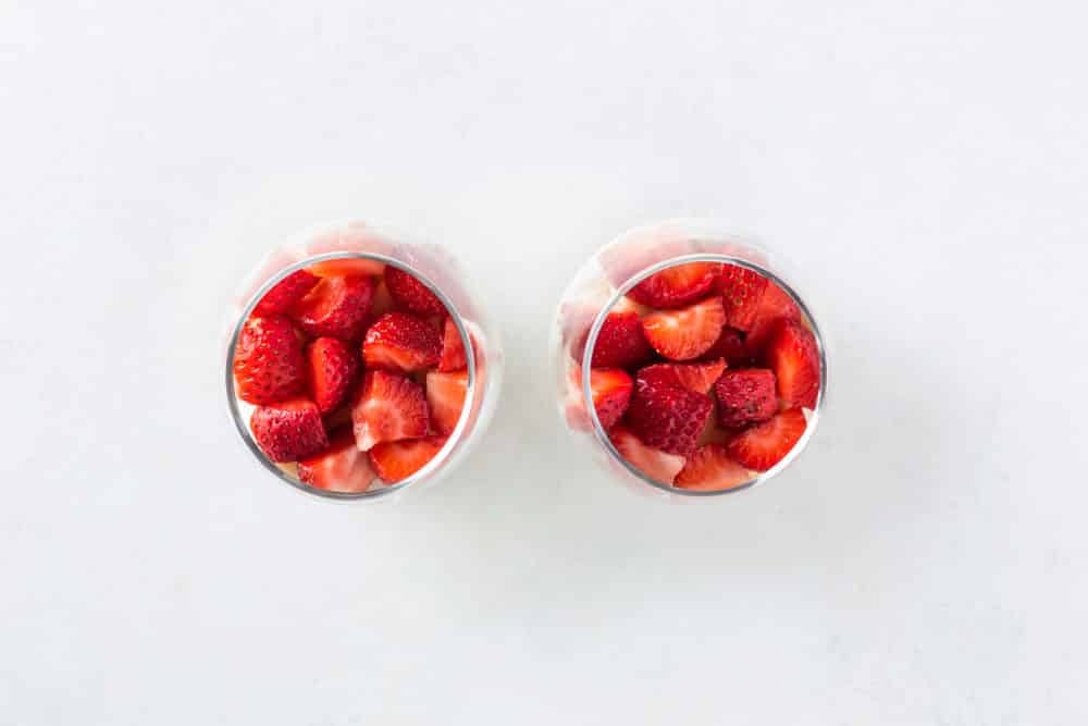 Two glass parfait cups with cut up strawberries on top.