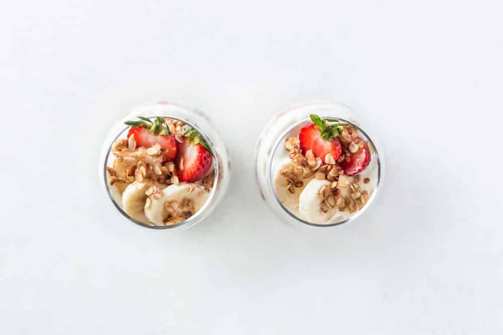Two glass parfait cups with granola yogurt sliced bananas and sliced strawberries.